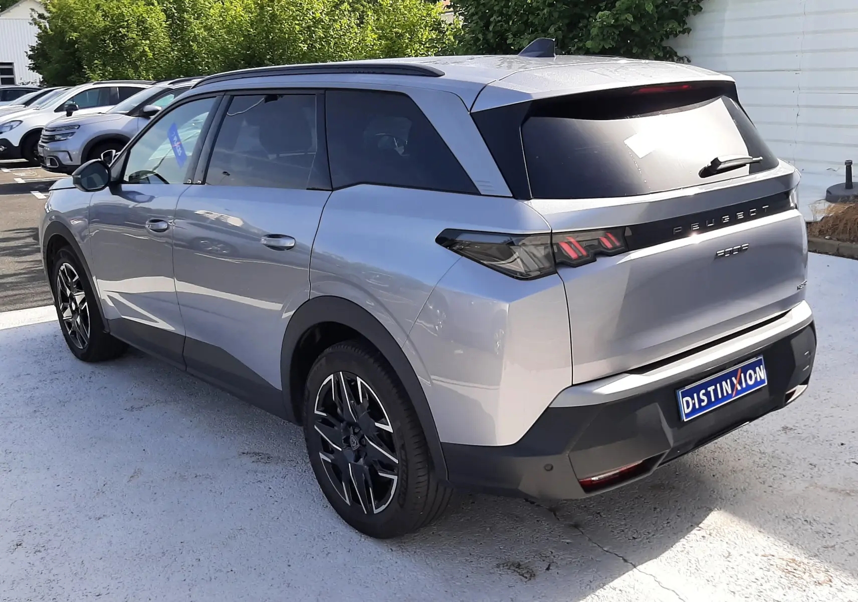 Peugeot 5008 Hybrid gris Artense métal en 3/4 arrière droit, avec feux arrière LED et jantes noires bicolores.
