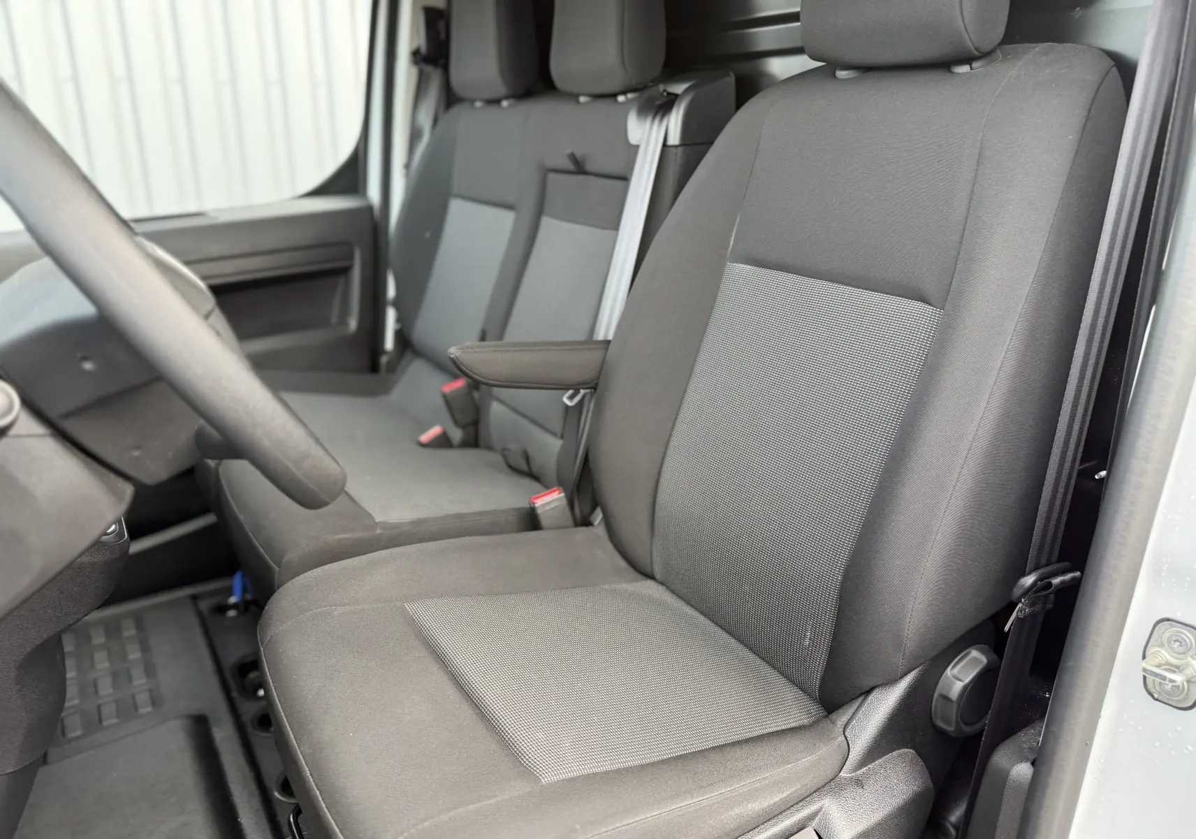 Vue intérieure côté conducteur du Fiat Scudo Fourgon 2025, sièges tissu gris foncé avec accoudoir central.