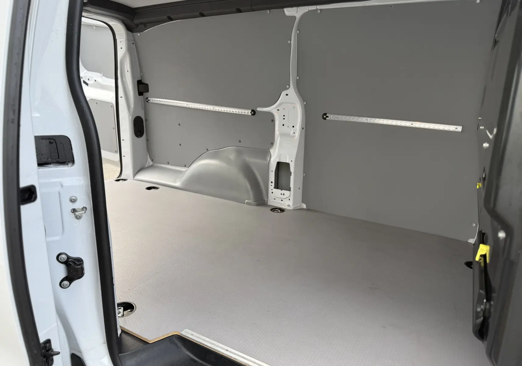 Intérieur du coffre du FIAT Scudo Fourgon blanc Icy, vue depuis la porte latérale ouverte, avec revêtement gris et fixations au sol.