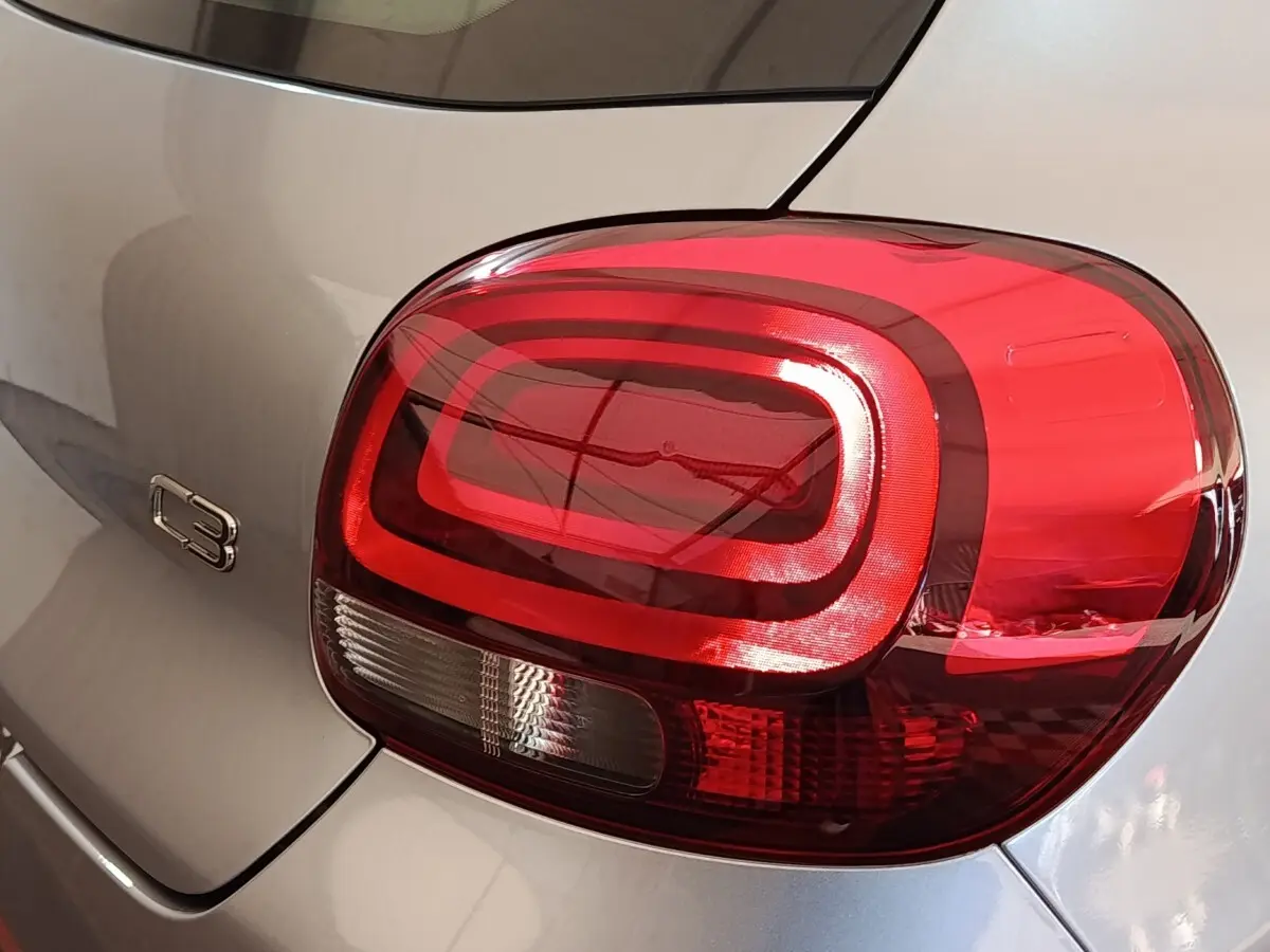Gros plan sur le feu arrière droit rouge et le logo C3 d'une Citroën C3 gris foncé vue de l'arrière.