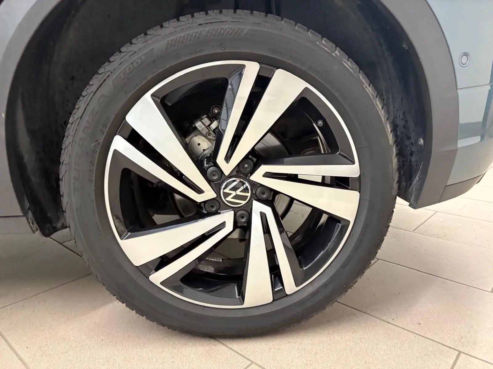 Gros plan sur la roue avant droite du Volkswagen T-Roc bleu pétrole, avec jante alliage bicolore et logo VW central.