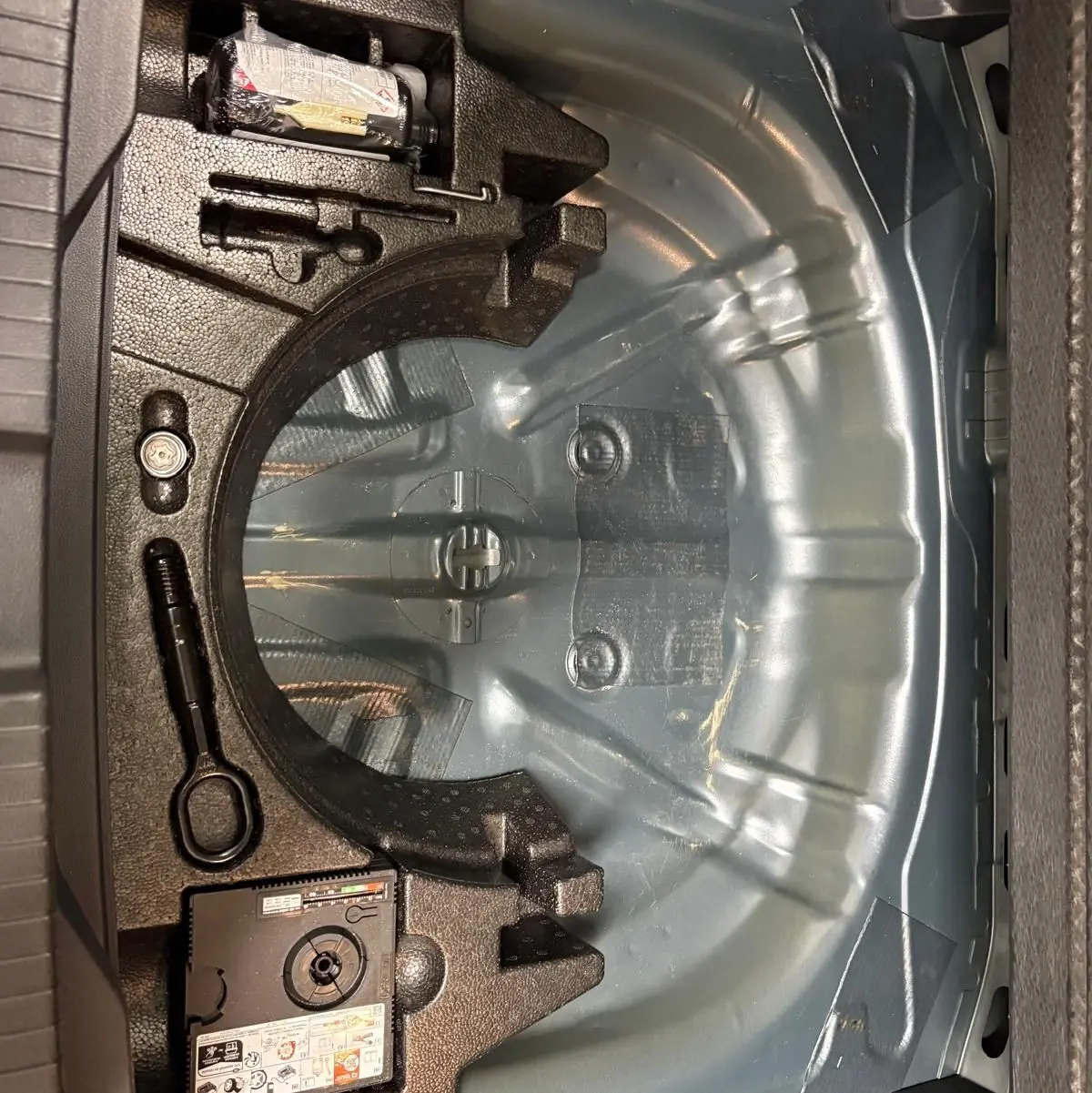 Coffre ouvert du Volkswagen T-Roc 2024 bleu pétrole, montrant le rangement pour roue de secours et outils intégrés.