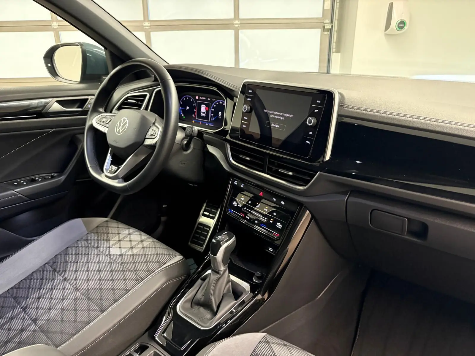 Intérieur du Volkswagen T-Roc 2024 vu côté conducteur, avec tableau de bord numérique et sellerie tissu gris à motifs.