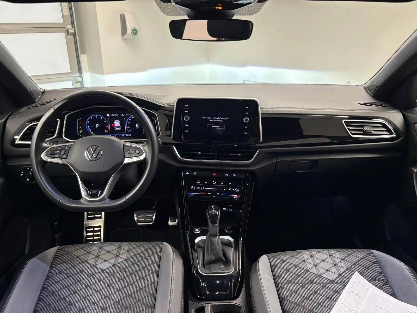 Vue intérieure avant du Volkswagen T-Roc 2024 avec tableau de bord moderne et sièges tissu gris à motifs.