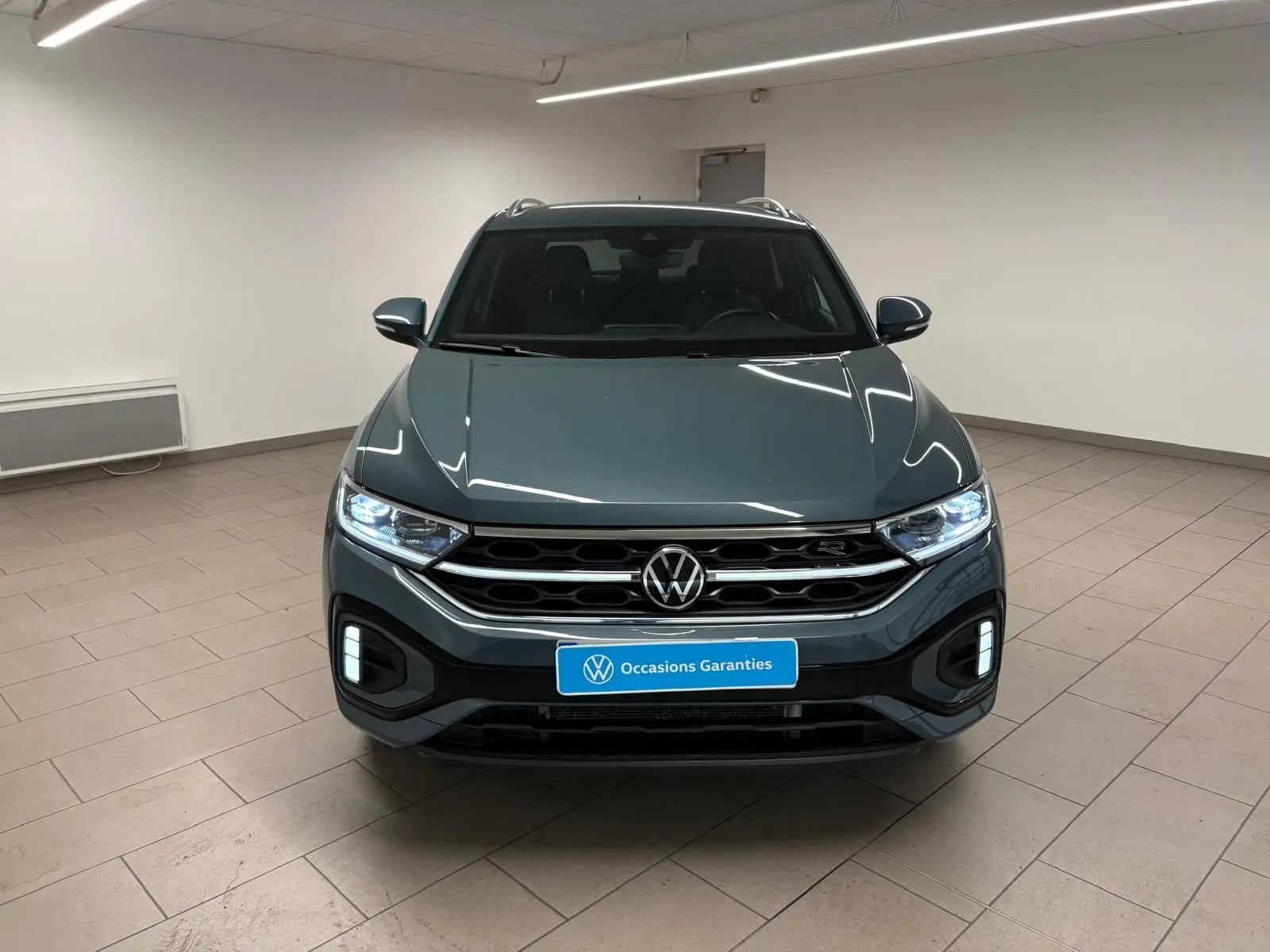 Volkswagen T-Roc 2024 bleu pétrole vu de face, avec projecteurs IQ.Light Matrix LED allumés et finition R-Line.