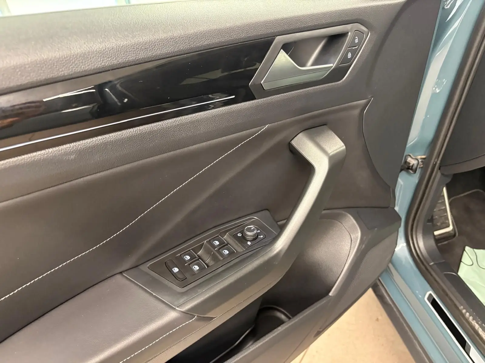 Détail de la porte avant gauche du Volkswagen T-Roc bleu pétrole 2024 avec commandes de vitres et serrure intégrées.