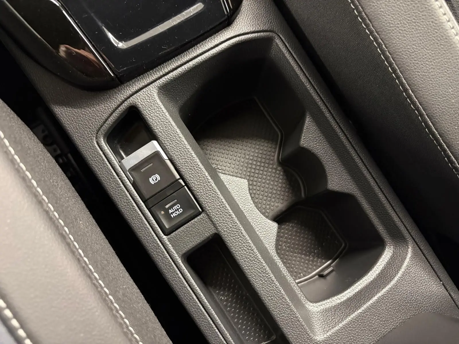 Gros plan sur la console centrale du Volkswagen T-Roc 2024, montrant les porte-gobelets et les commandes de frein à main électrique.
