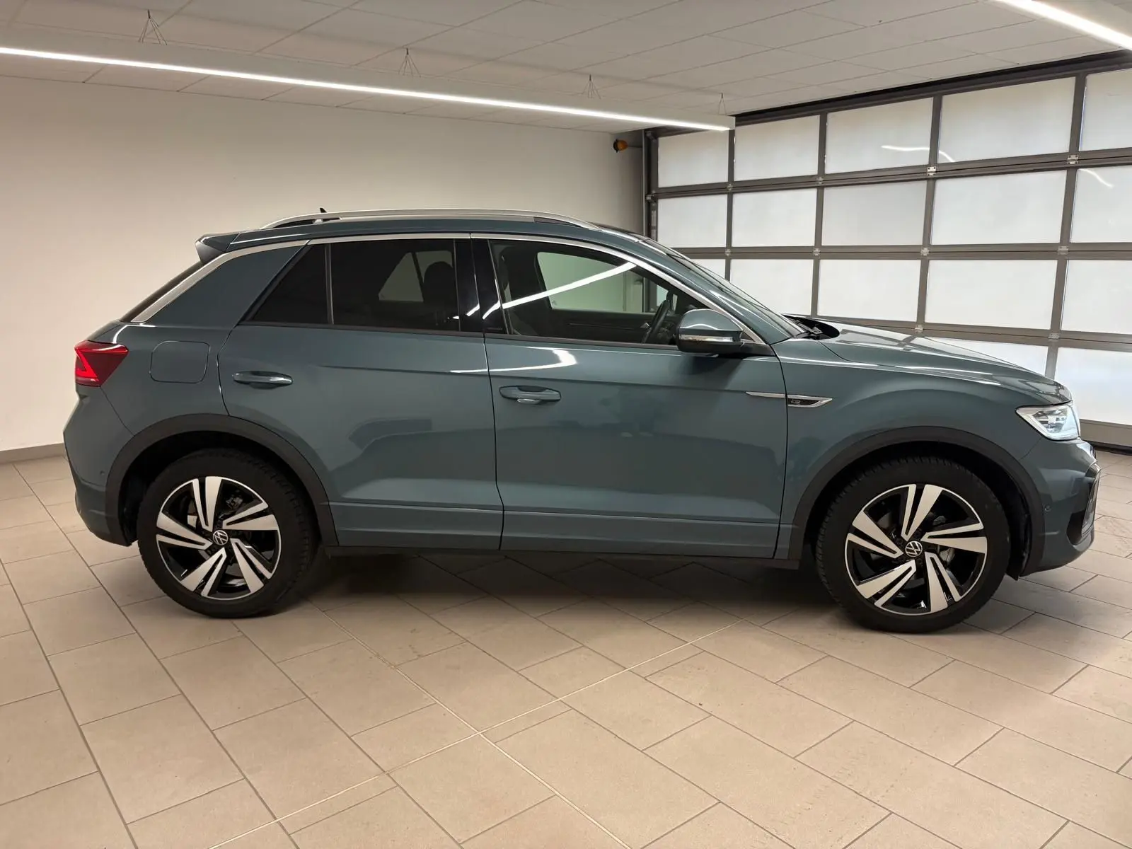 Volkswagen T-Roc 2024 bleu pétrole vu de profil côté gauche avec jantes R-Line et vitres teintées.