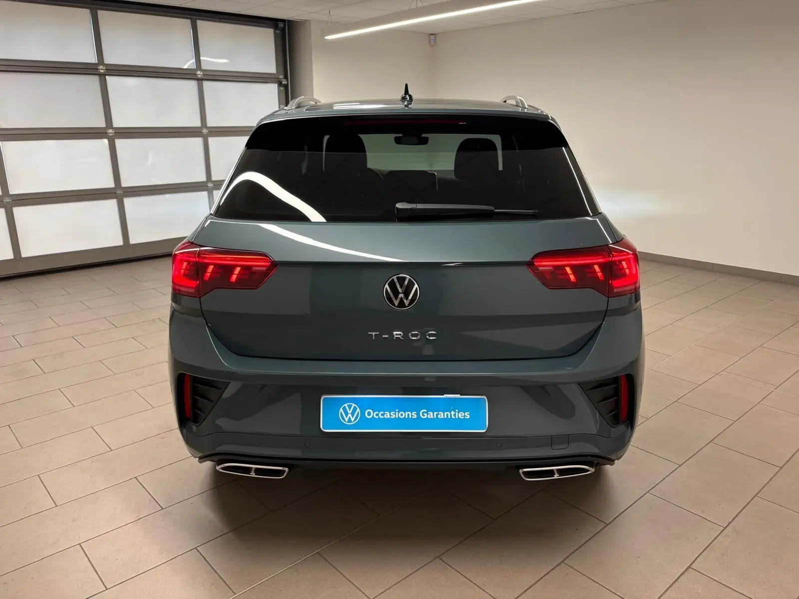 Vue arrière d'un Volkswagen T-Roc 2024 bleu pétrole avec feux LED allumés et double sortie d'échappement rectangulaire.