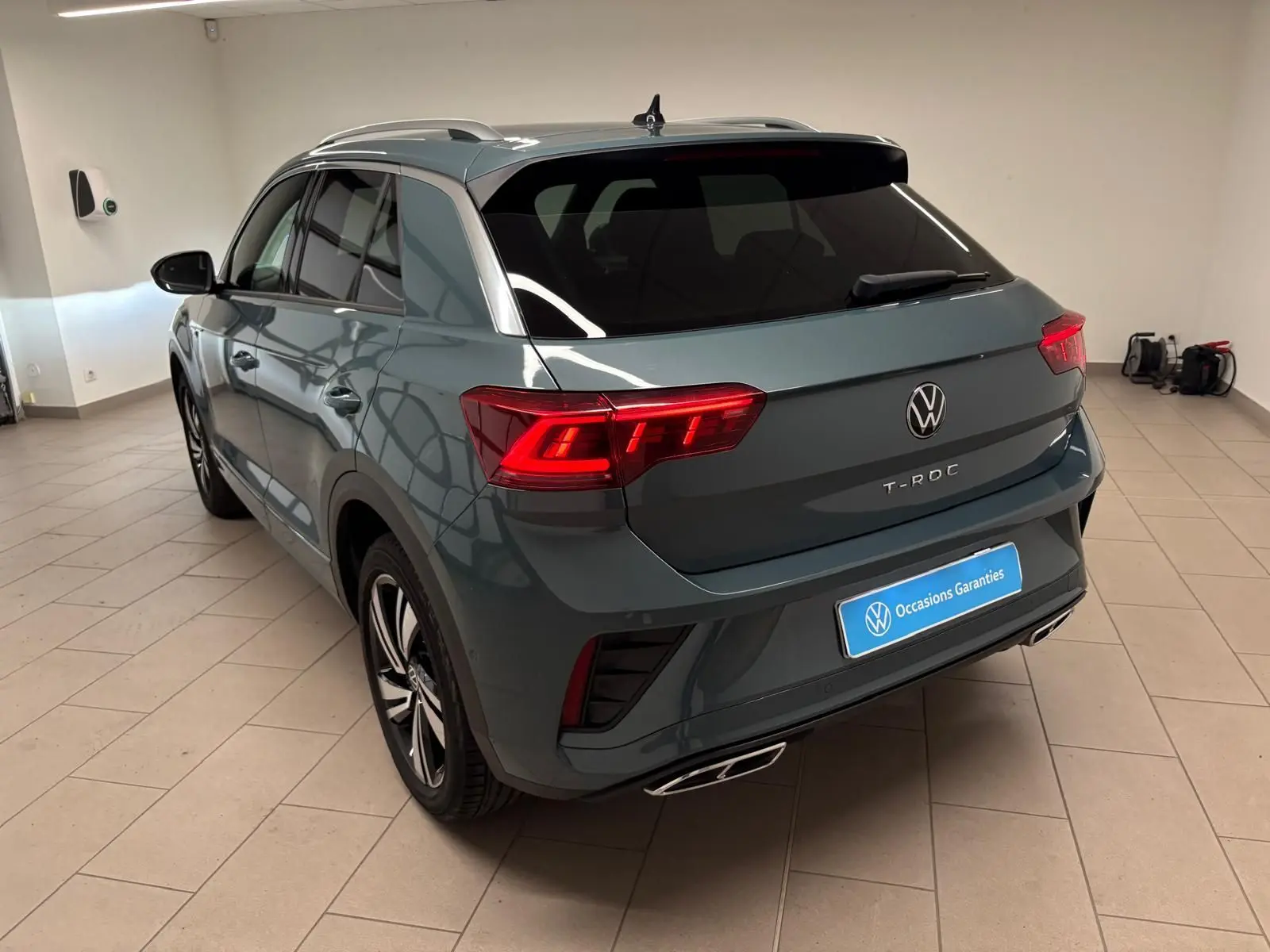 Volkswagen T-Roc bleu pétrole en 3/4 arrière droit, avec feux LED Matrix et finition R-Line visible en intérieur.