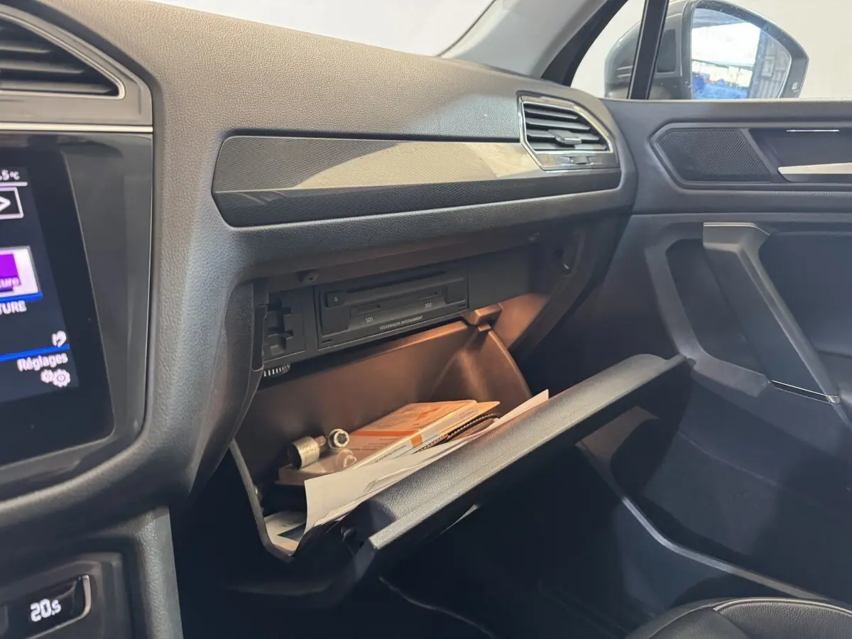Intérieur côté passager du Volkswagen Tiguan Allspace gris, boîte à gants ouverte avec documents visibles.