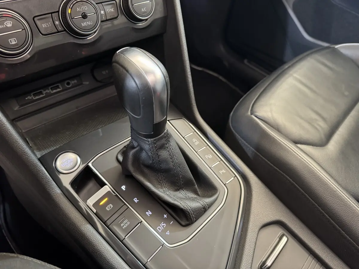 Vue rapprochée de la console centrale du Volkswagen Tiguan Allspace gris foncé, montrant le levier de vitesse automatique et les commandes environnantes.