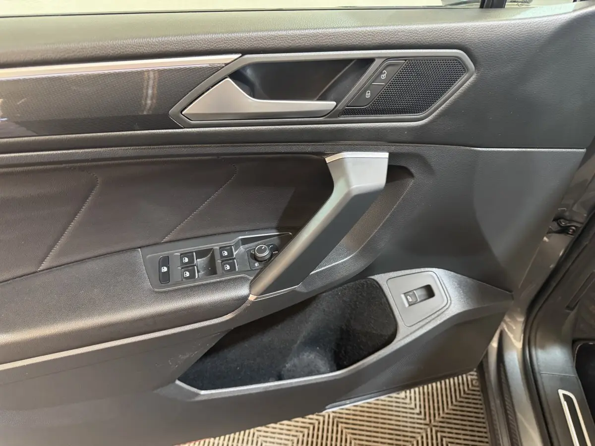 Vue rapprochée de la porte avant gauche du Volkswagen Tiguan Allspace gris foncé, avec commandes de vitres et poignée argentée.