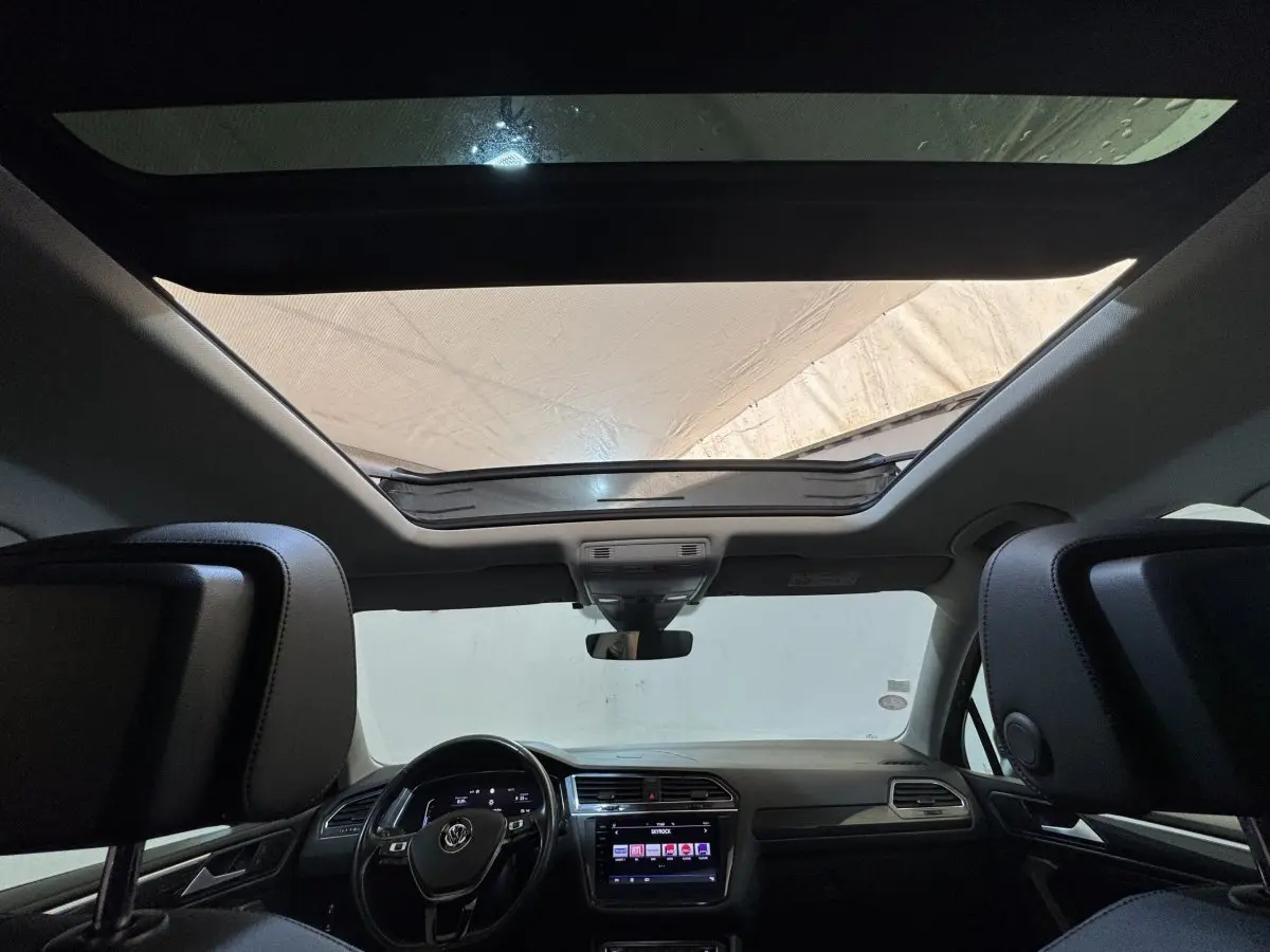 Vue intérieure avant du Volkswagen Tiguan Allspace gris foncé, avec toit ouvrant panoramique et tableau de bord moderne.