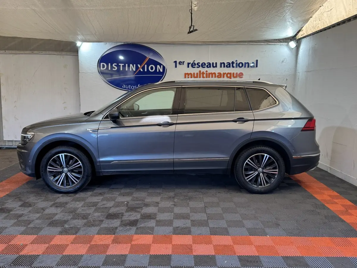 Vue de profil côté gauche d'un Volkswagen Tiguan Allspace gris foncé avec jantes alliage, dans un showroom intérieur.