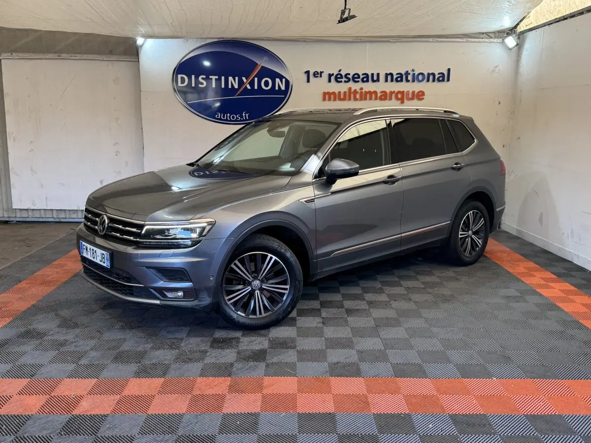 Volkswagen Tiguan Allspace gris foncé en 3/4 avant droit, avec jantes alliage et barres de toit chromées.