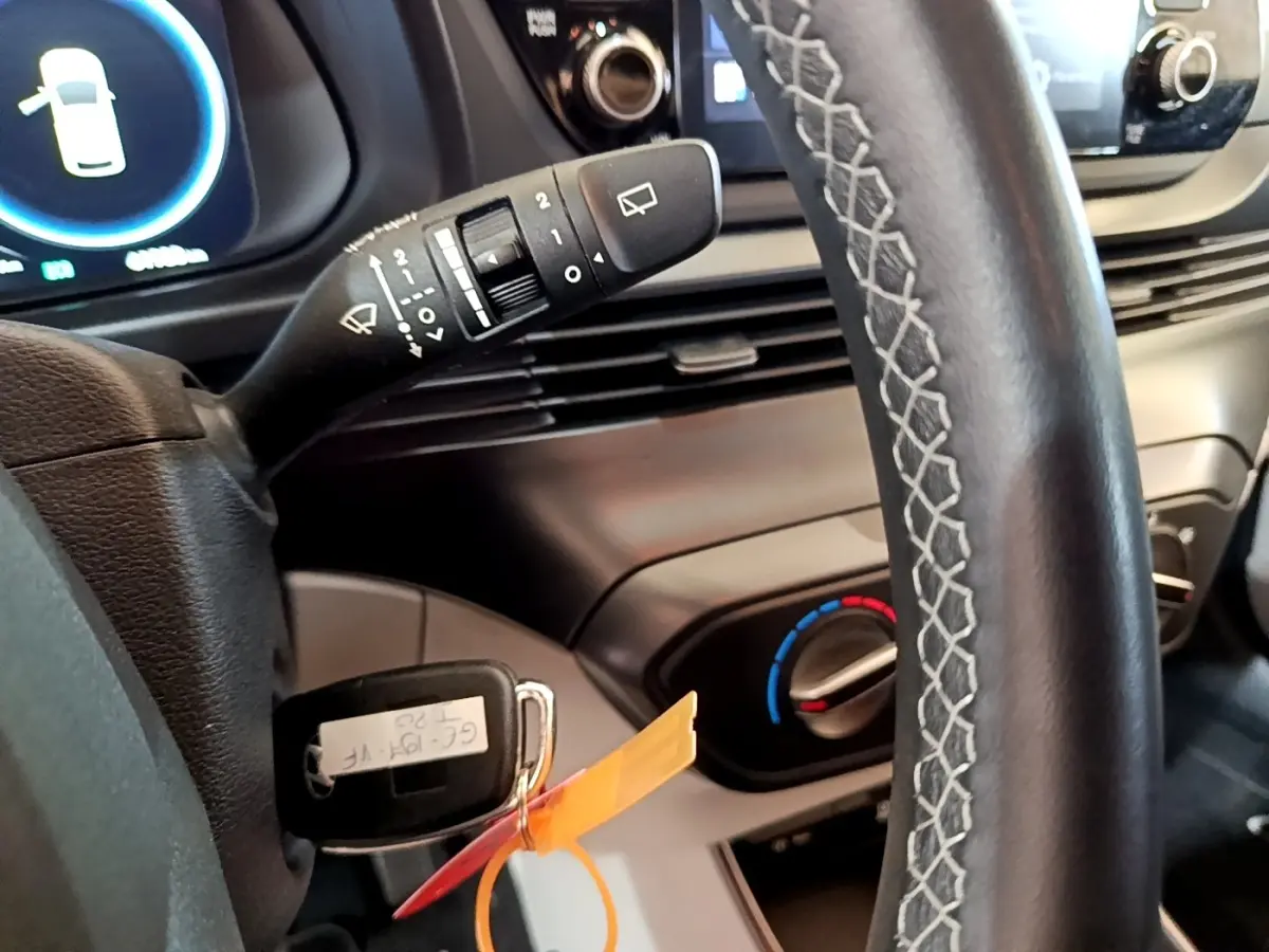 Gros plan sur le volant cuir et la clé insérée du Hyundai i20 gris clair, avec commandes d’essuie-glace et réglage clim visible.