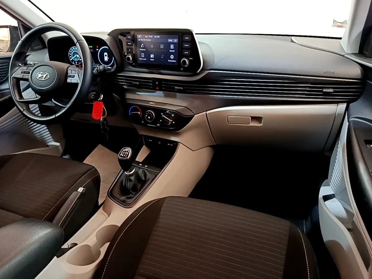 Vue intérieure de la Hyundai i20 2022, tableau de bord gris clair avec volant cuir multifonctions et boîte manuelle.