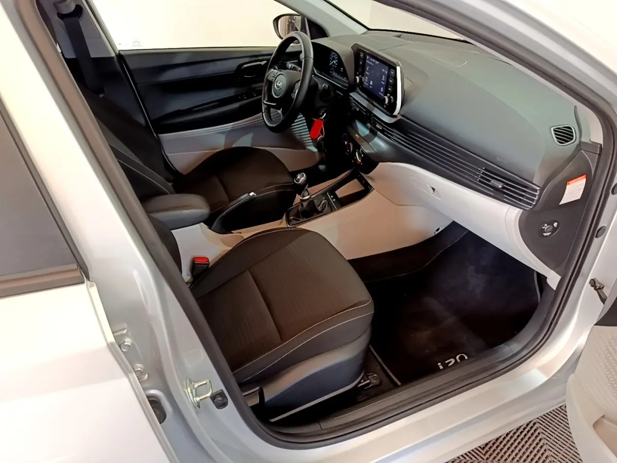 Vue intérieure côté conducteur de la Hyundai i20 gris clair 2022, avec tableau de bord moderne et volant multifonctions cuir.