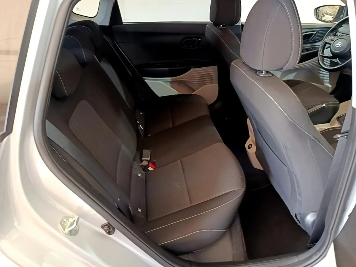 Vue intérieure côté gauche montrant les sièges arrière noirs et partie avant avec volant cuir d'une Hyundai i20 gris clair 2022.