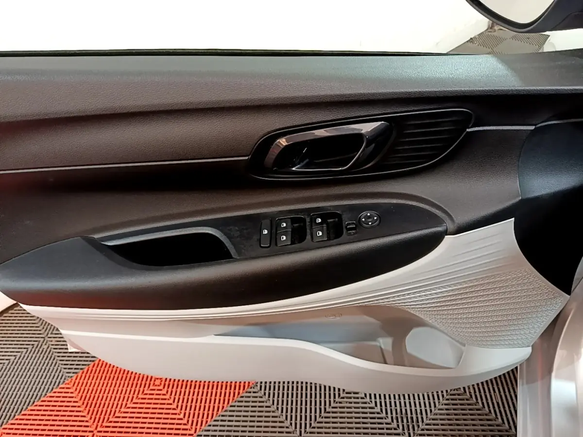 Vue intérieure du panneau de porte côté conducteur de la Hyundai i20 gris clair, avec commandes électriques et poignée noire.