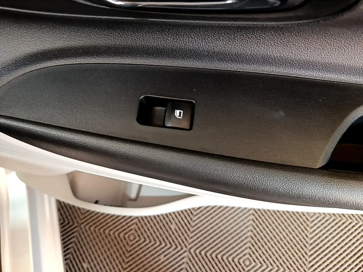 Gros plan sur le bouton de verrouillage des portes dans la portière intérieure noire d'une Hyundai i20 gris clair.