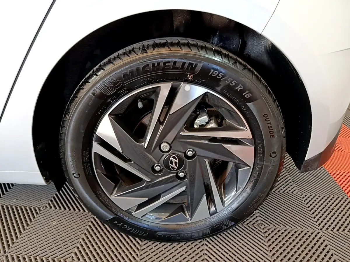 Gros plan sur la roue arrière droite d'une Hyundai i20 gris clair, avec jante alliage au design géométrique.