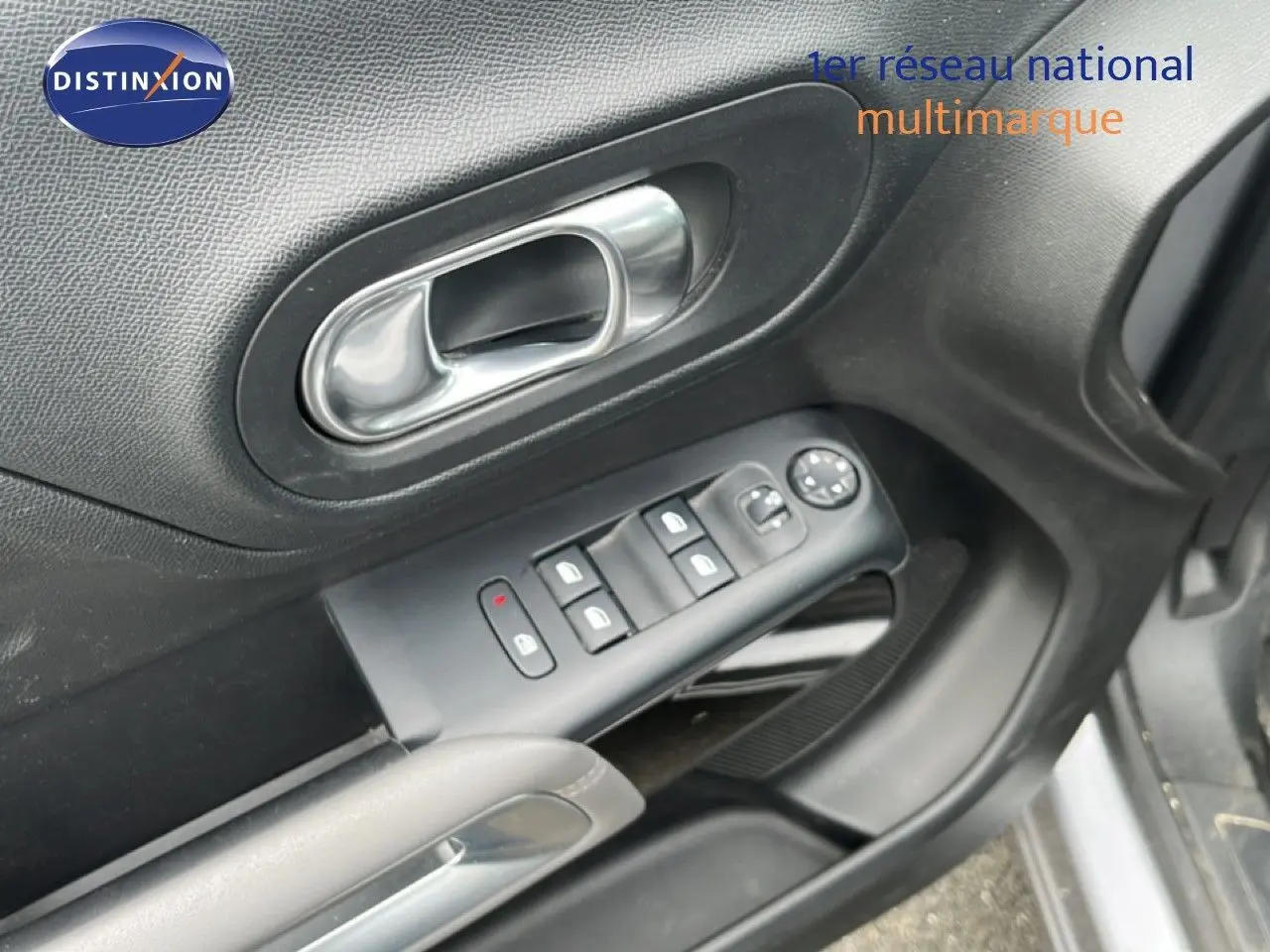 Gros plan sur la commande des vitres et la poignée intérieure côté conducteur d’une Citroën C5 Aircross gris clair.