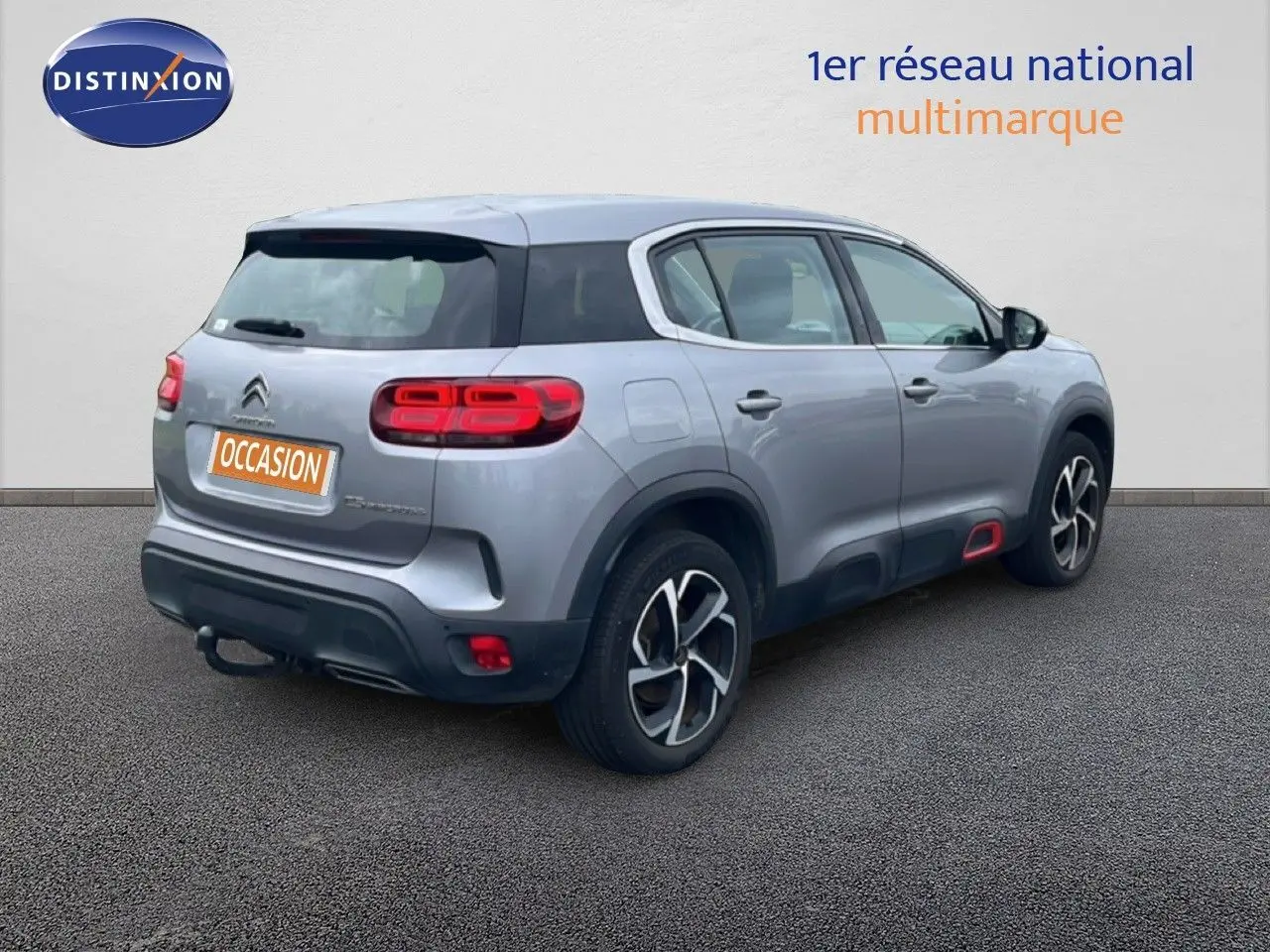 Vue 3/4 arrière droite d'un Citroën C5 Aircross gris clair métal avec jantes noires et détails rouges sur le bas de caisse.