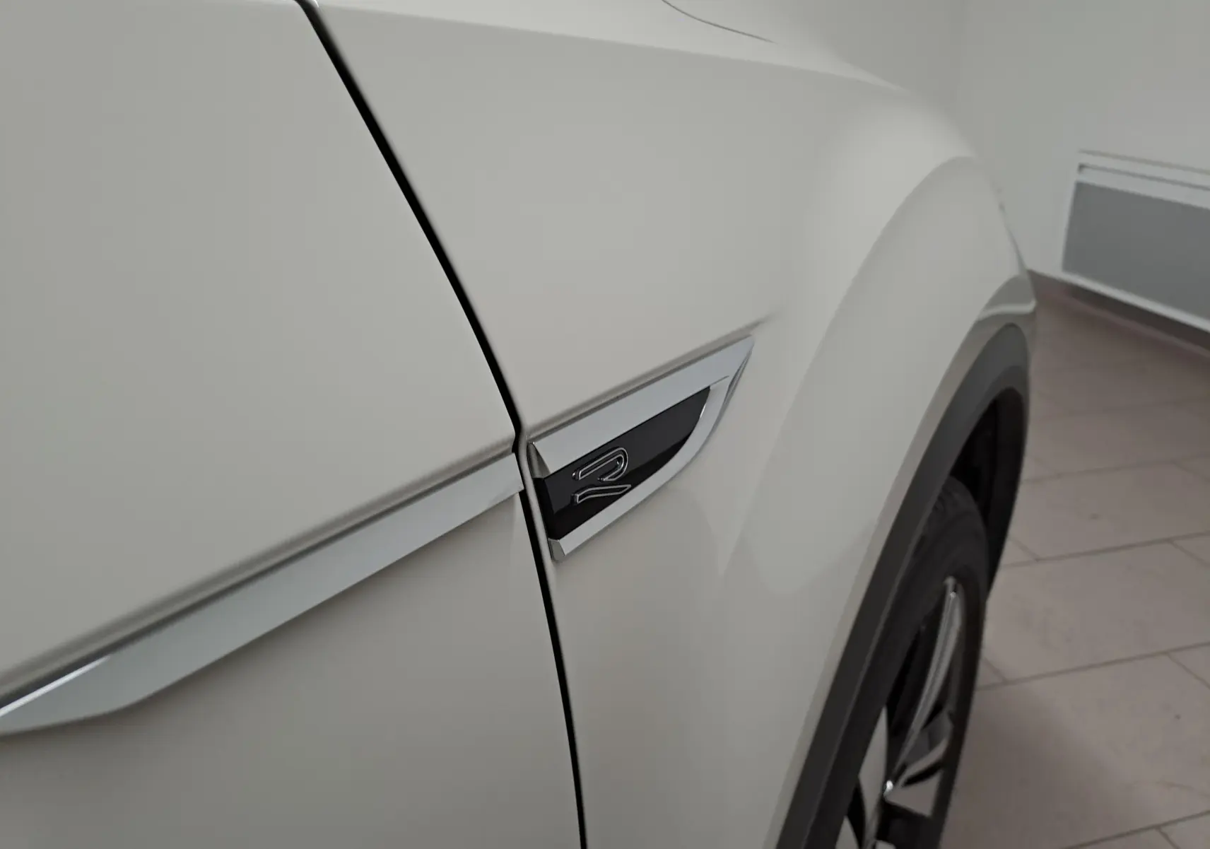 Gros plan sur l'aile avant droite gris Ascot du Volkswagen T-Roc 2024 avec logo R-Line et jante visible.