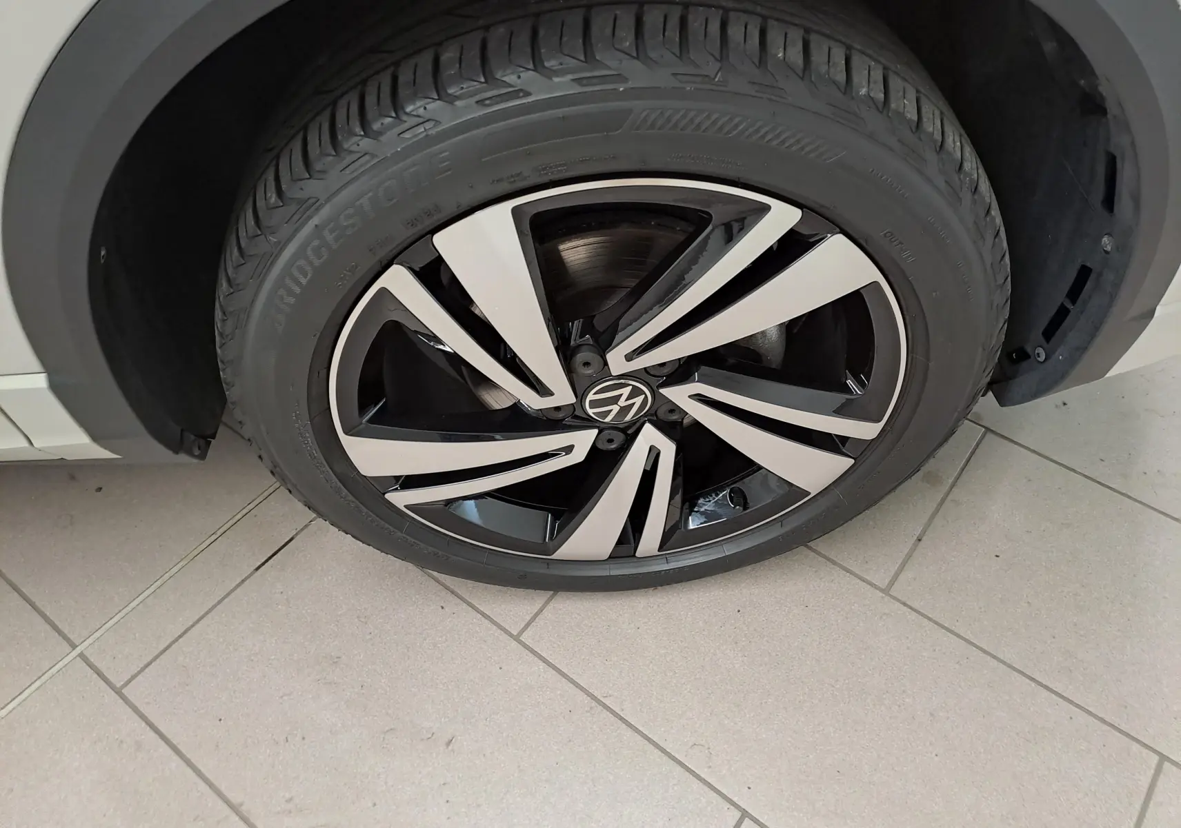 Gros plan sur la roue avant gauche du Volkswagen T-Roc 2024 Gris Ascot avec jante alliage bicolore au design dynamique.
