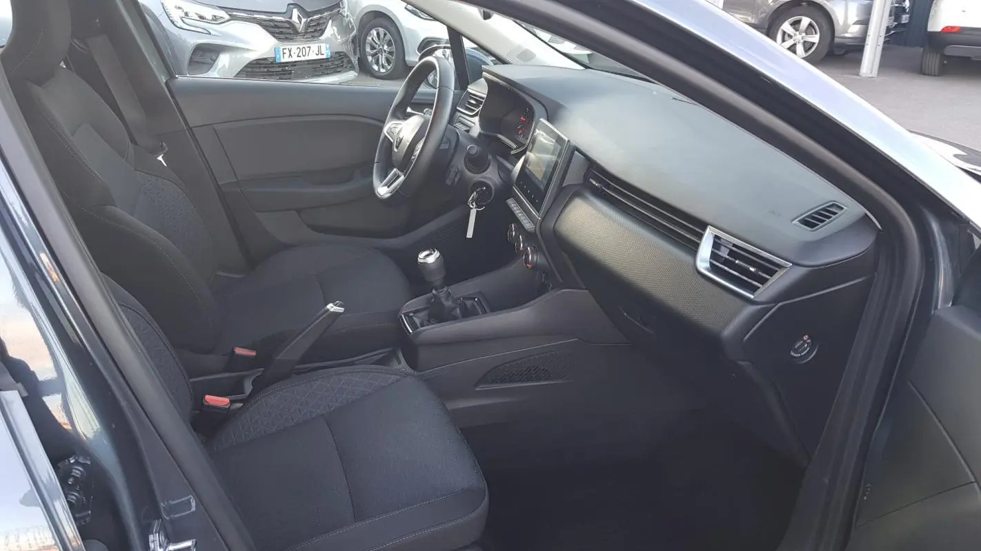 Intérieur de la Renault Clio gris 2021, vue côté conducteur montrant sièges noirs et tableau de bord moderne.