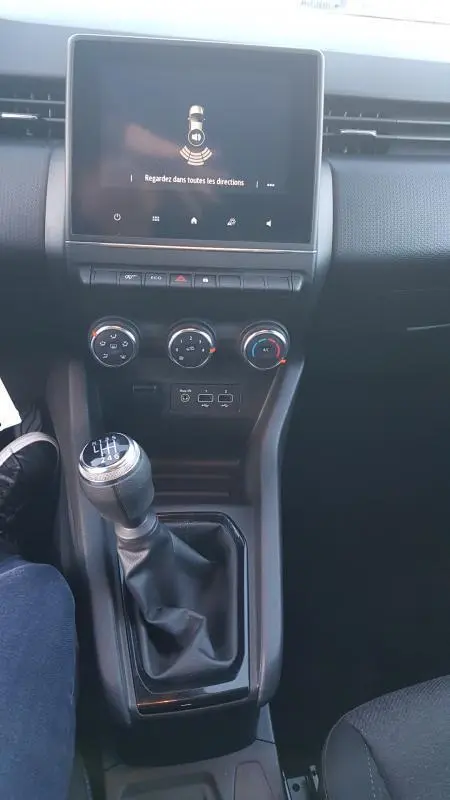 Vue intérieure centrée sur la console centrale d'une Renault Clio 2021, avec levier de vitesses manuel et écran tactile allumé.