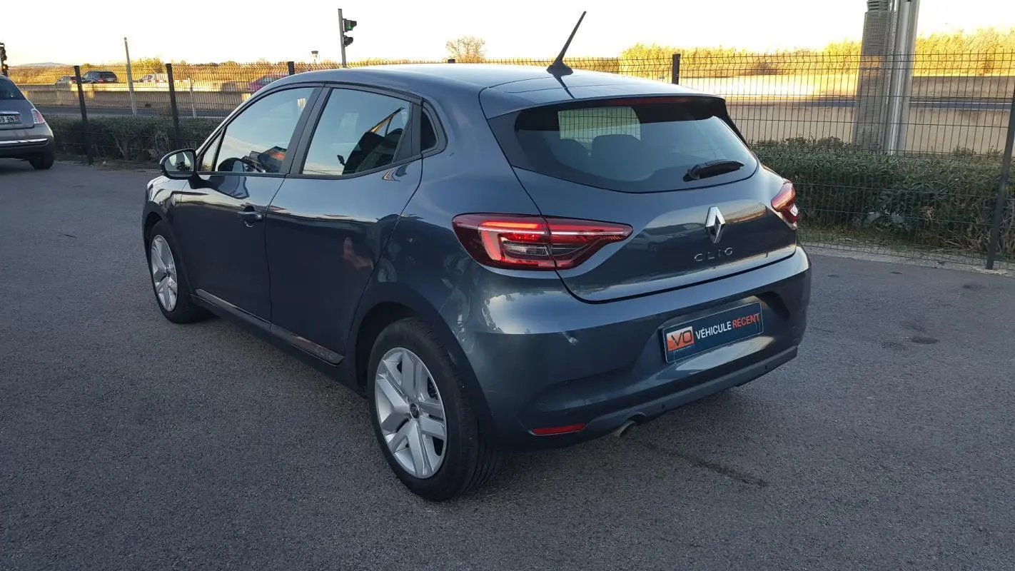 Renault Clio gris vue 3/4 arrière droit, avec feux arrière allumés et jantes alliage visibles.