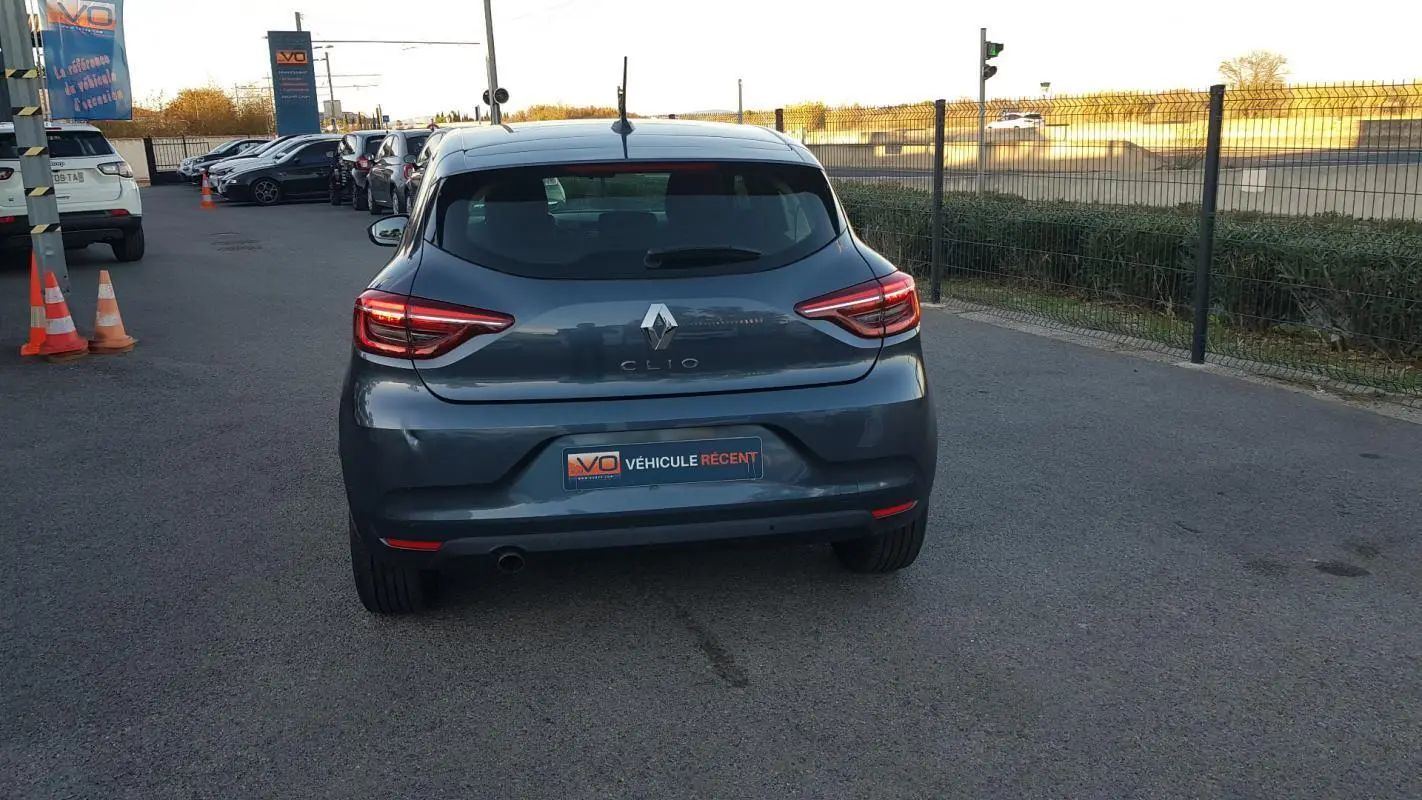 Vue arrière d'une Renault Clio gris foncé 2021, avec feux arrière allumés sur un parking extérieur.