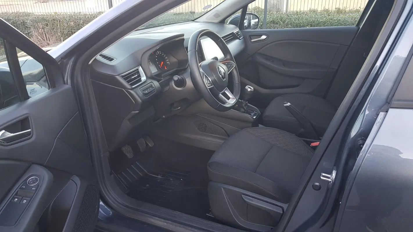 Intérieur côté conducteur d'une Renault Clio gris 2021, montrant le volant, tableau de bord et sièges noirs.