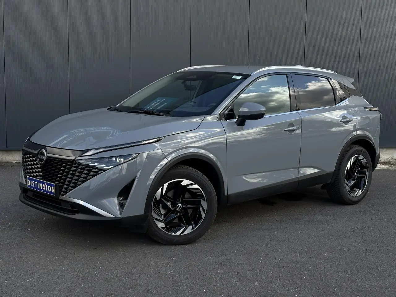 Nissan Qashqai 2025 gris Ceramic en 3/4 avant droit, avec jantes alliage noires et calandre distinctive.