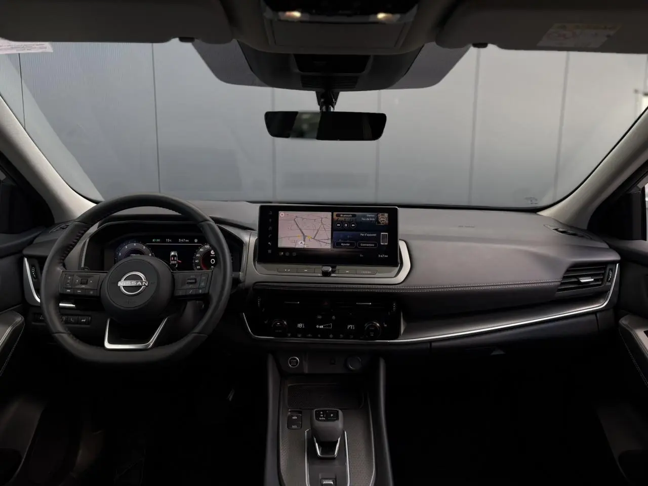 Vue frontale de l’habitacle du Nissan Qashqai 2025, tableau de bord noir avec écran tactile central et volant cuir.