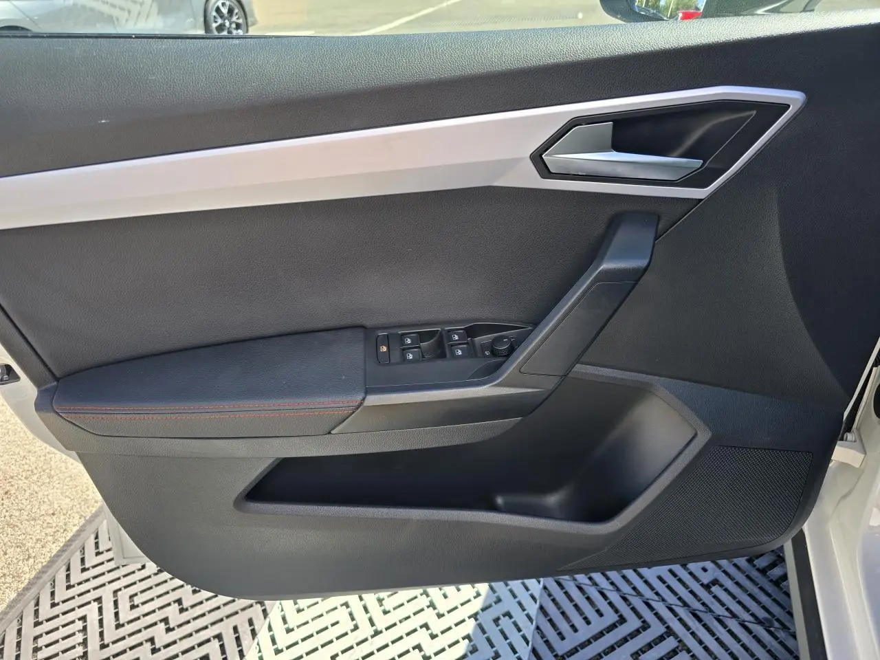 Vue intérieure de la porte avant gauche d'une SEAT Arona blanche, avec garniture noire et surpiqûres rouges.