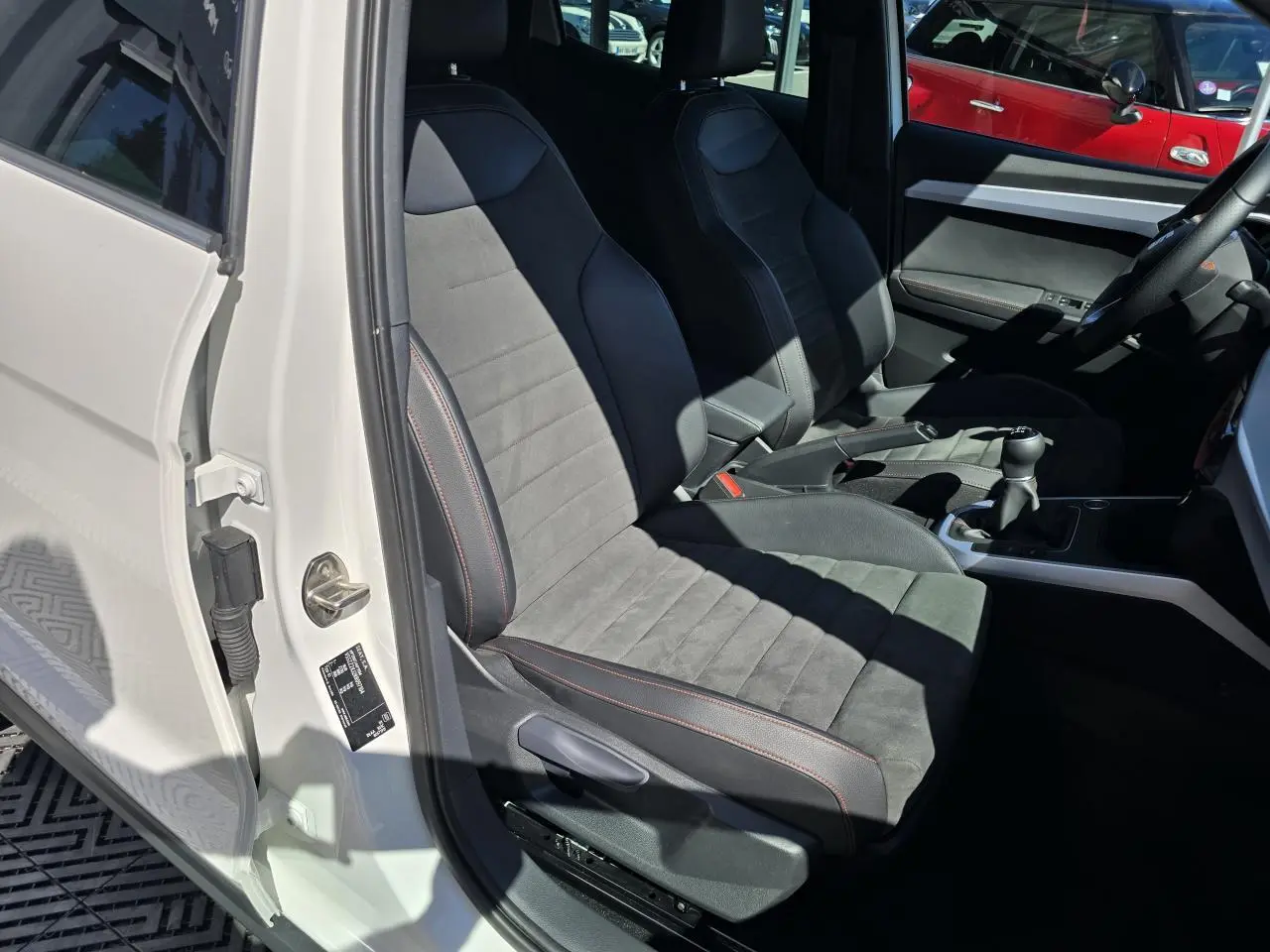 Vue intérieure côté conducteur du SEAT Arona blanc toit noir 2024, sièges en suédine noire avec surpiqûres rouges et boîte manuelle.