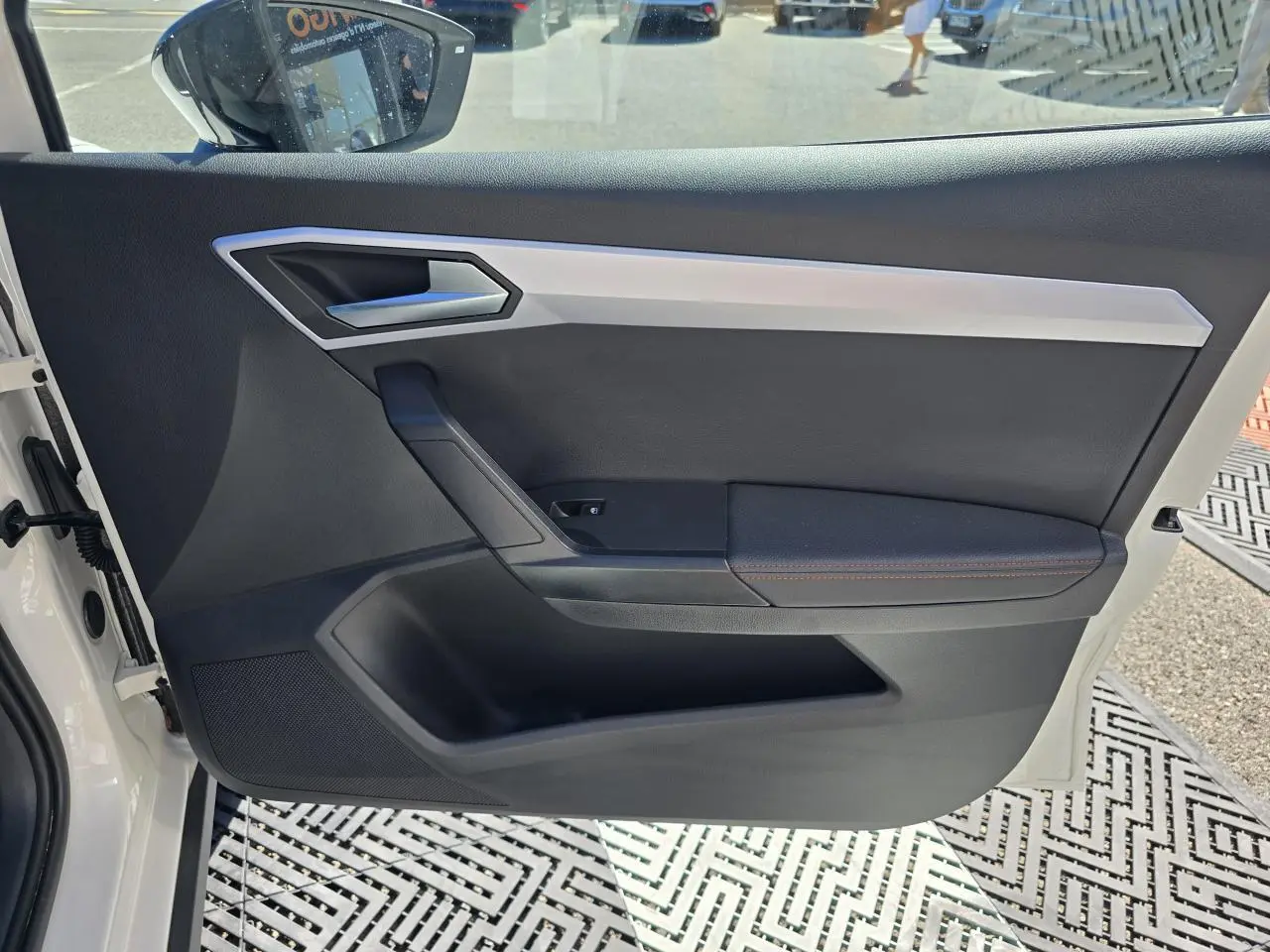 Vue intérieure de la porte avant gauche d'une SEAT Arona 2024 blanc toit noir, avec garniture noire et surpiqûres rouges.