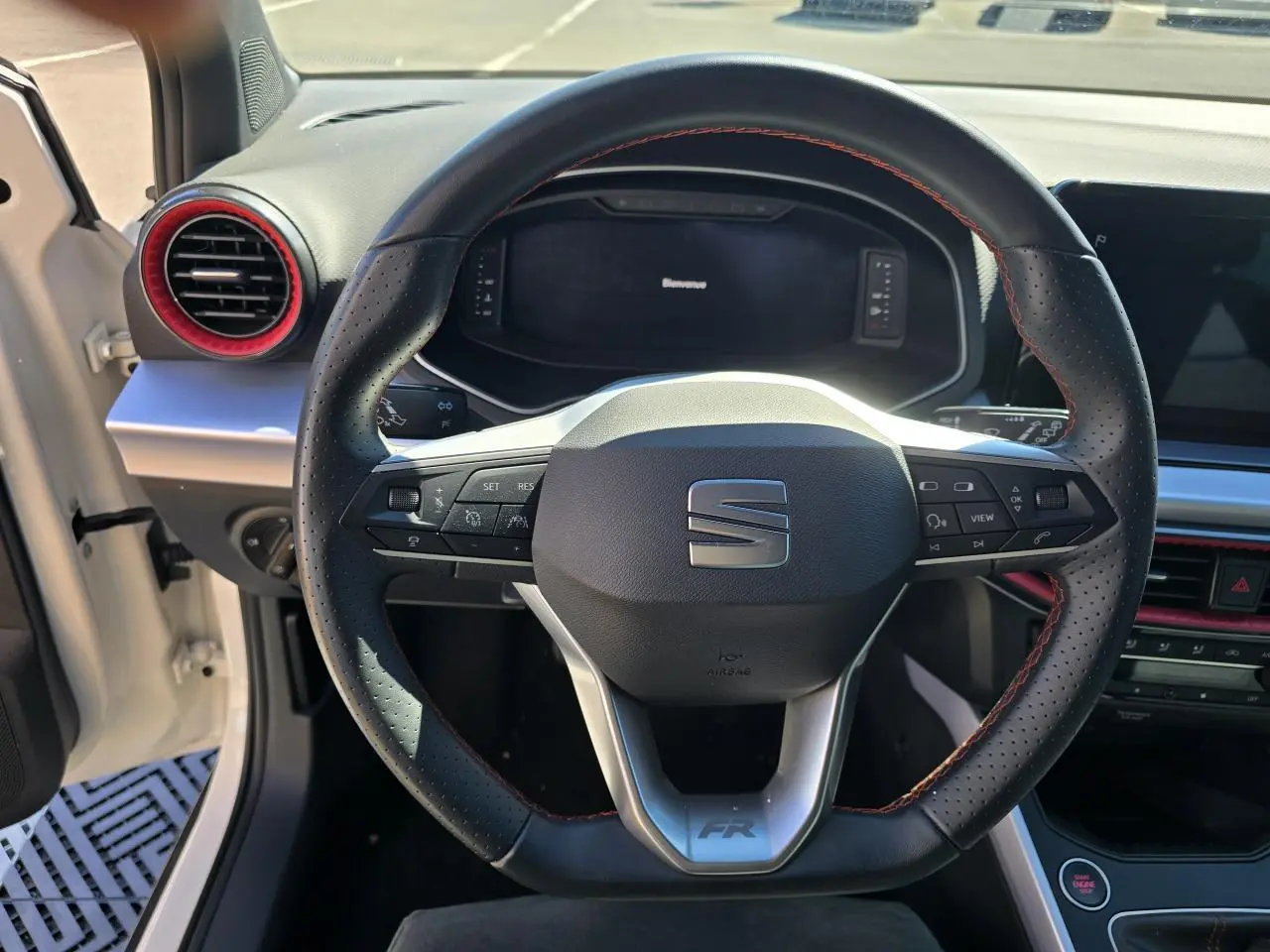 Vue rapprochée du volant sport en cuir noir avec surpiqûres rouges du SEAT Arona blanc toit noir, tableau de bord et aérateurs rouges visibles.