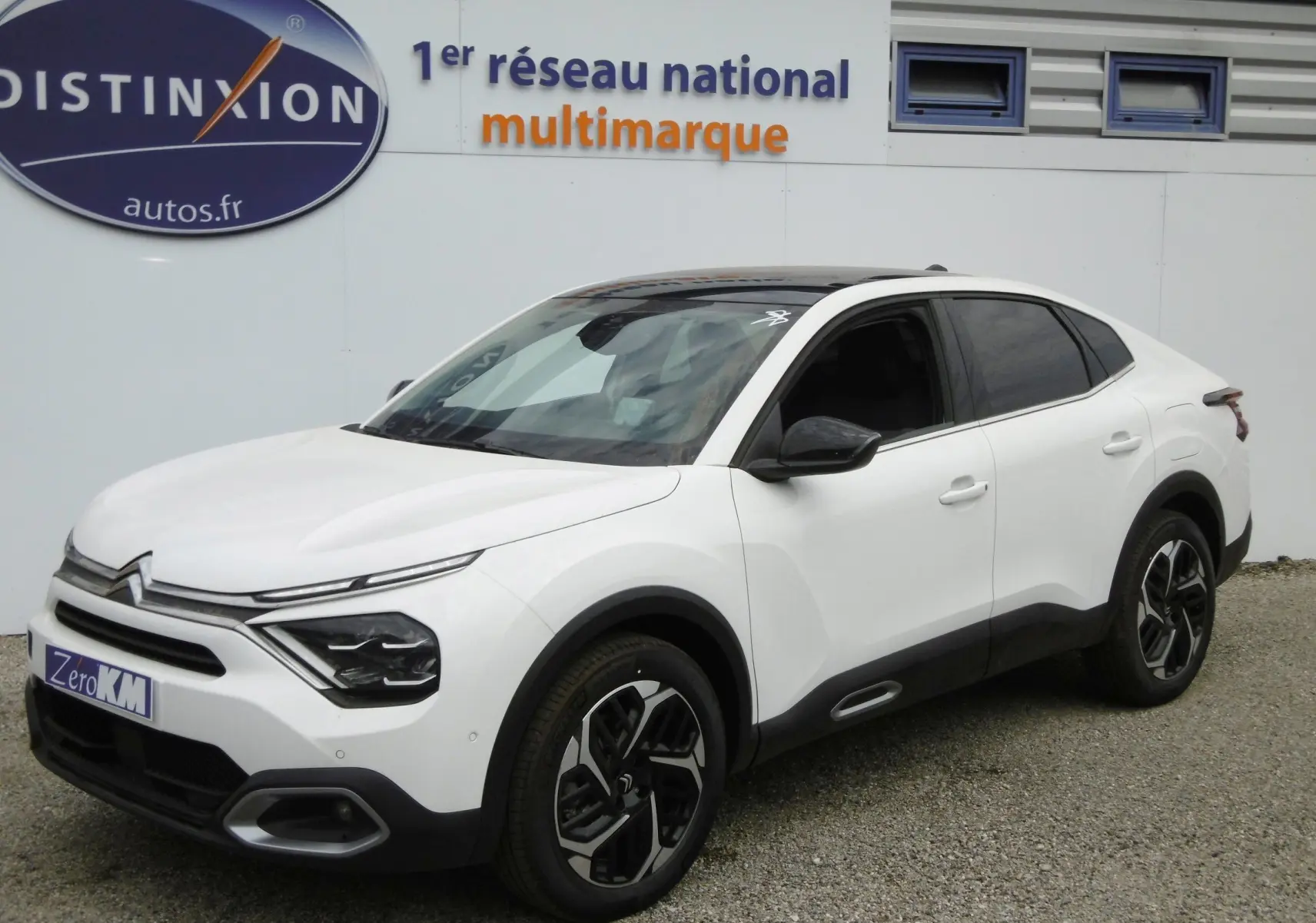 Citroën C4 X blanc polaire en 3/4 avant droit, avec jantes bicolores et vitres teintées sur parking extérieur.