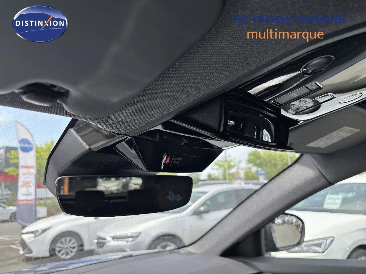 Vue intérieure du rétroviseur central et du plafonnier du Renault Austral bleu iron avec toit noir, en stationnement extérieur.