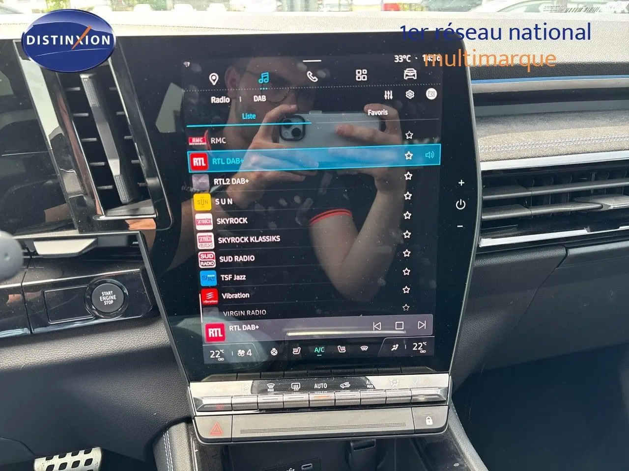 Vue rapprochée de l'écran tactile central du Renault Austral 2024 bleu iron, affichant les stations radio avec commandes climatisation en dessous.