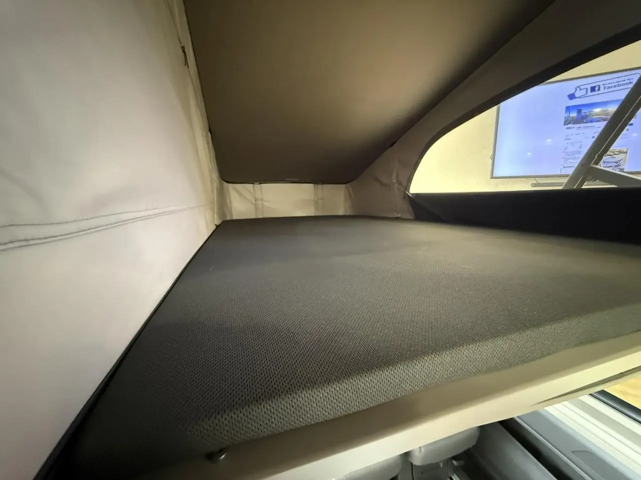 Vue intérieure du couchage supérieur du Volkswagen California T7 2024 avec toit relevable et matelas gris.