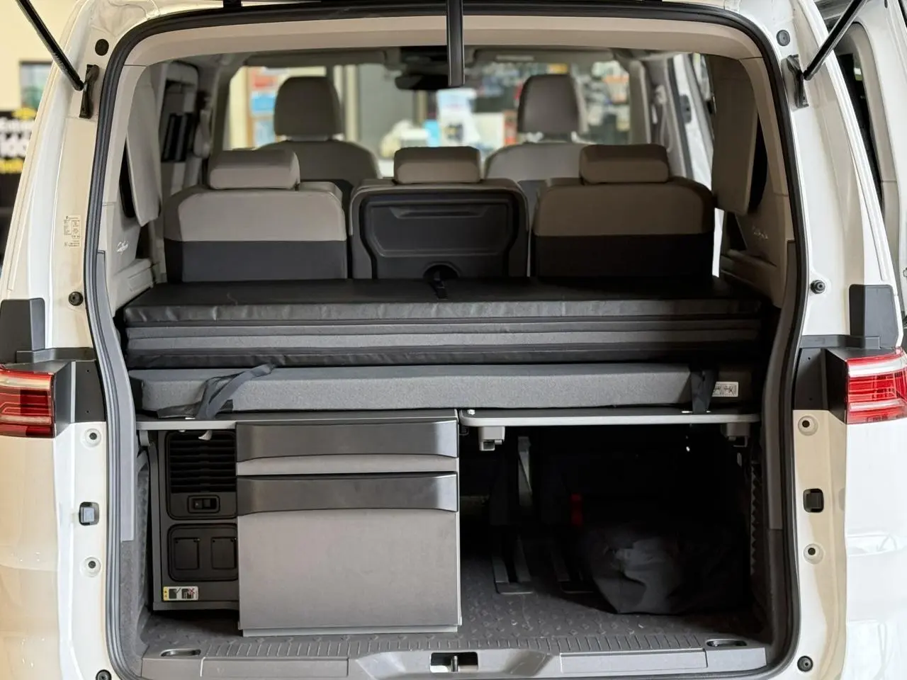 Vue arrière ouverte du Volkswagen California T7 blanc Candy, montrant la banquette et la mini-cuisine intégrée.