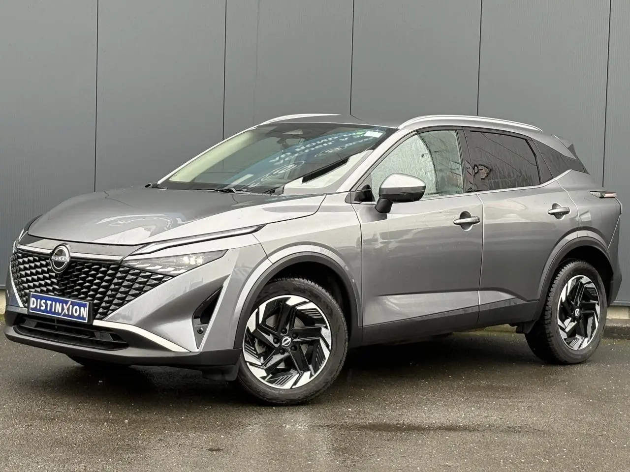 Nissan Qashqai 2024 gris Squale en 3/4 avant droit, avec calandre noire texturée et jantes alliage 18 pouces.