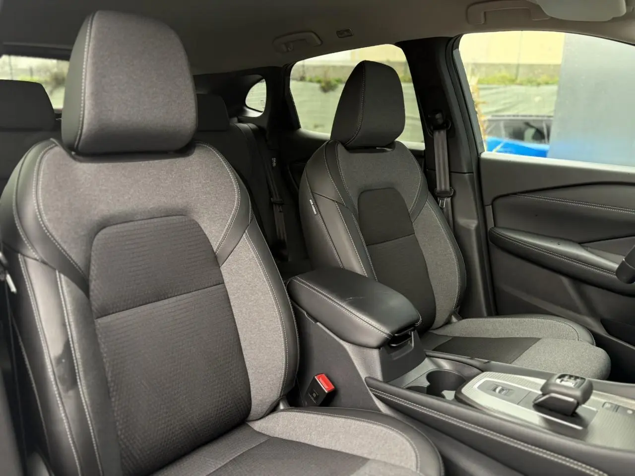 Vue intérieure des sièges avant gris clair et noir du Nissan Qashqai 2024, avec accoudoir central et console moderne.