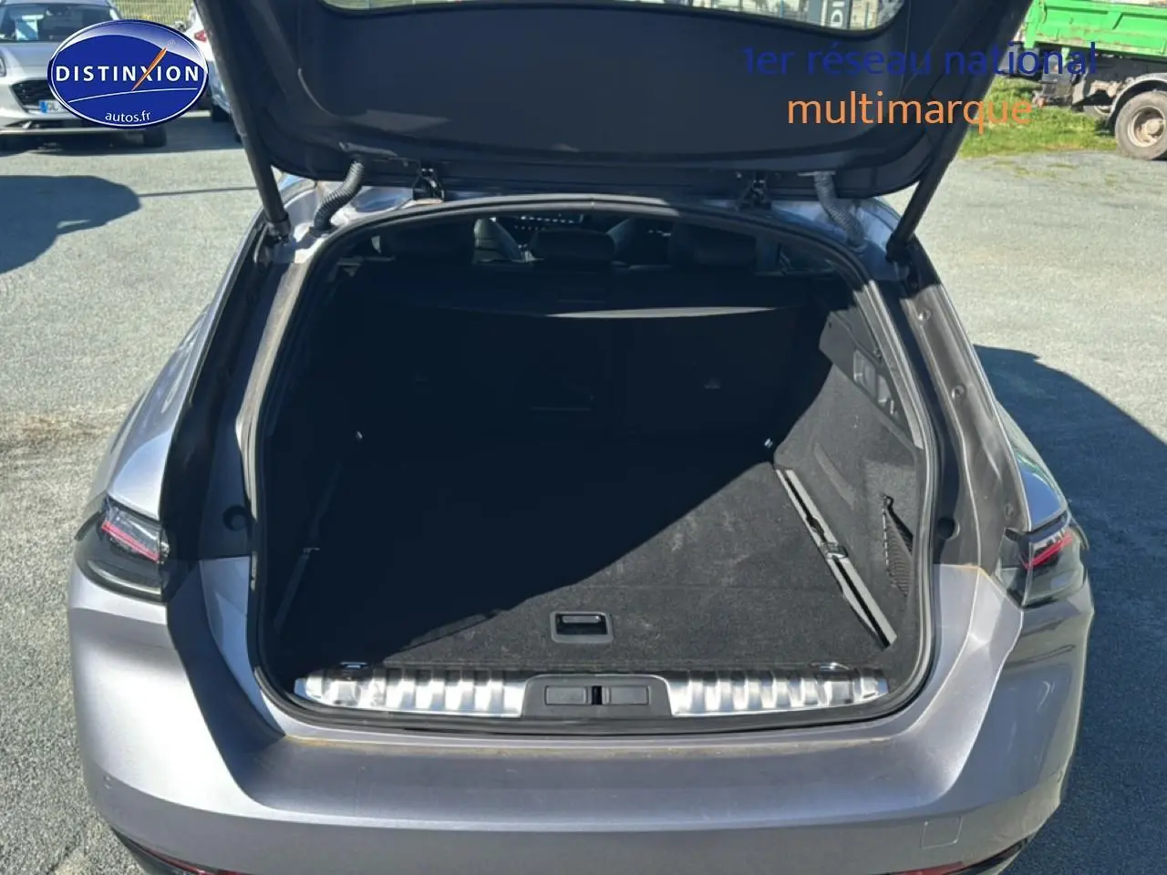 Coffre ouvert vu de l'arrière d'une Peugeot 508 SW Hybrid 225 gris artense, avec hayon relevé et espace de chargement vide.